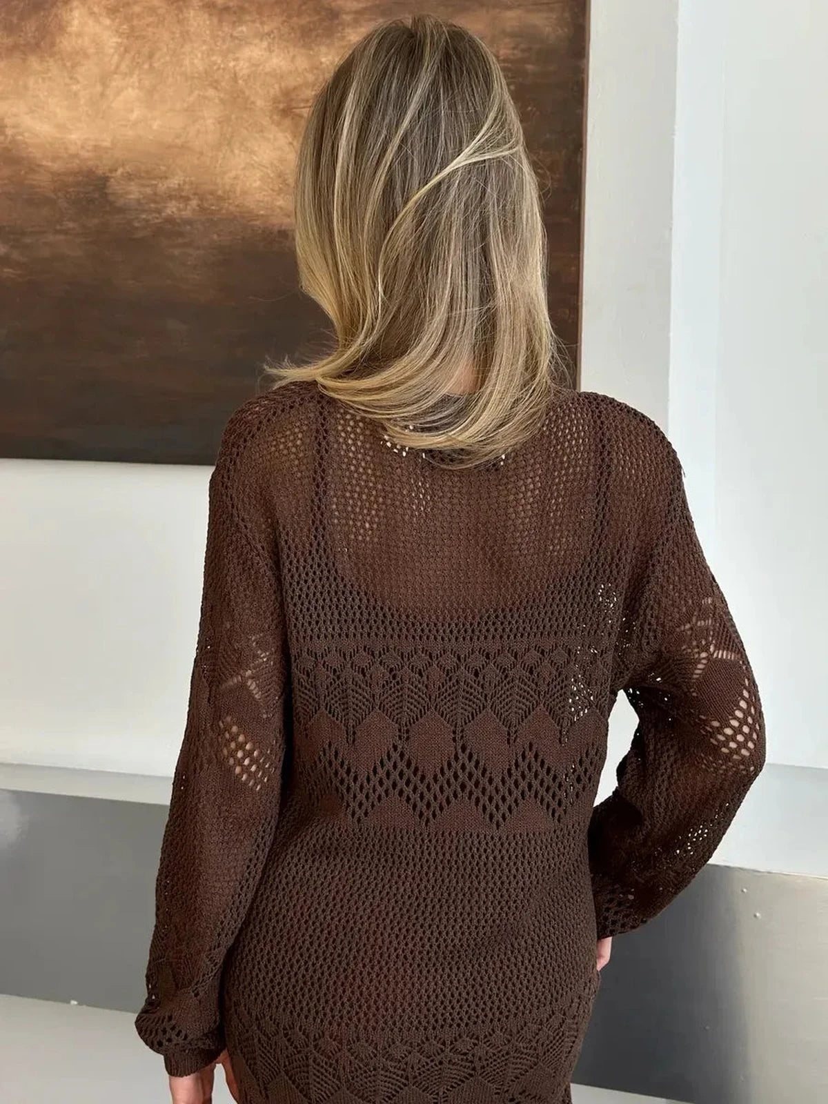 Rear view of a model wearing the Solara Maxi Dress by Lauven, showcasing its warm dark brown crochet knit design.