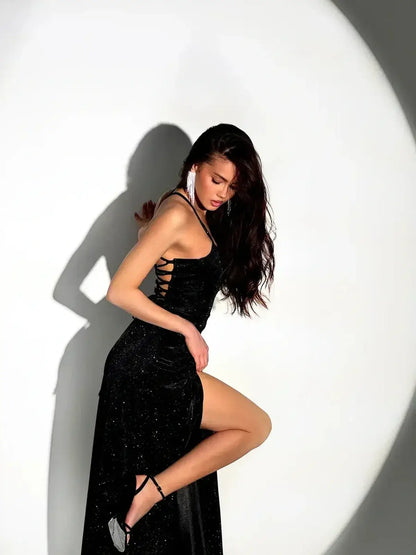 Model in a shimmering black Starlight Maxi Dress with a high slit, showcasing strappy allure and glamour.