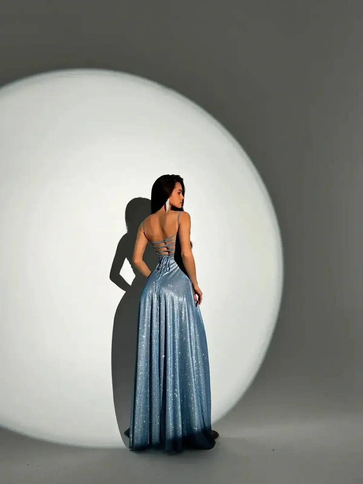 Model showcasing the Starlit Glow Maxi Dress in shimmer-blue under dramatic lighting, highlighting its elegant silhouette.