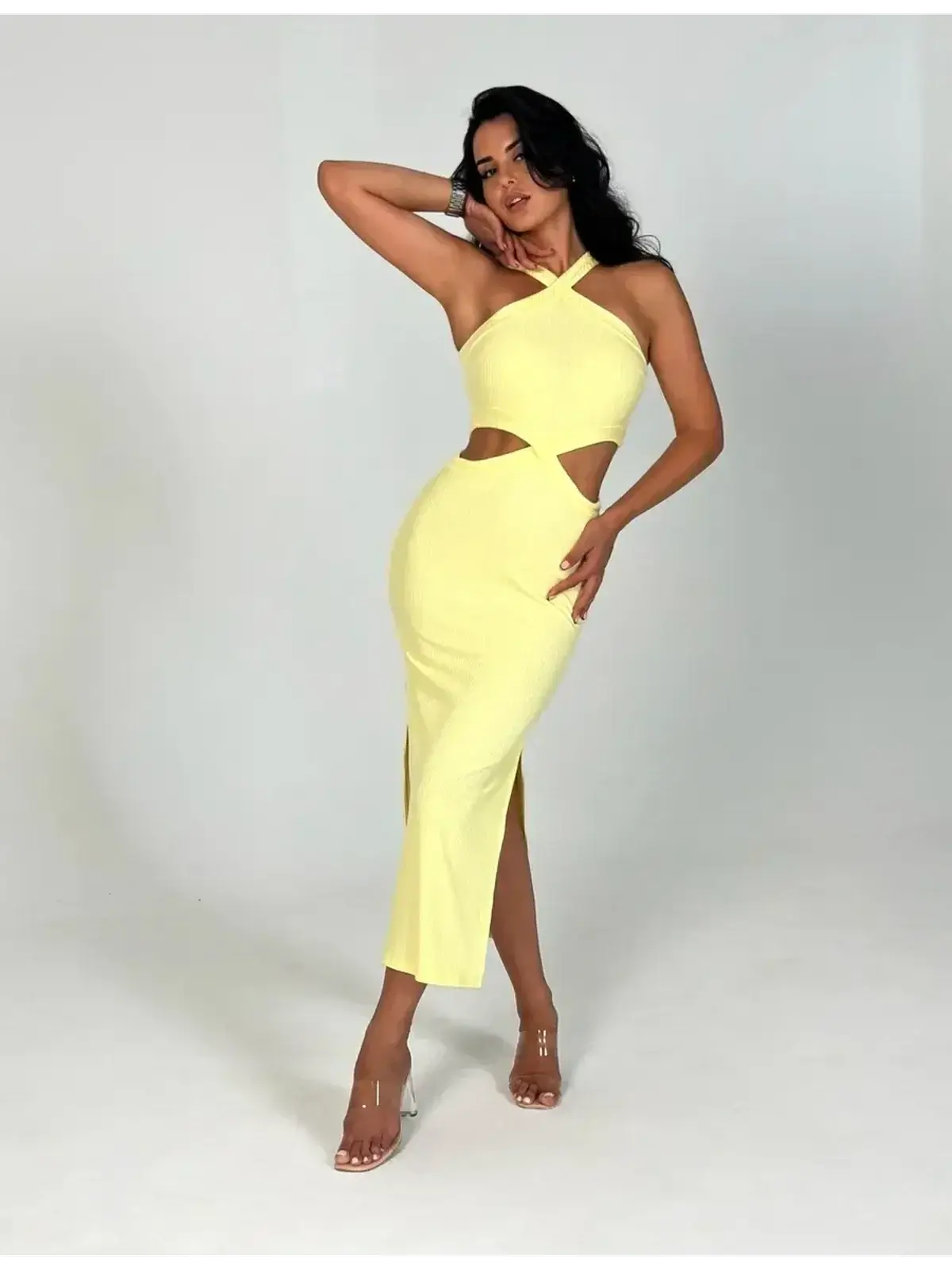 Woman wearing a Sunlace Midi Dress in pastel yellow, showcasing sculptural cutouts and a sleek silhouette.