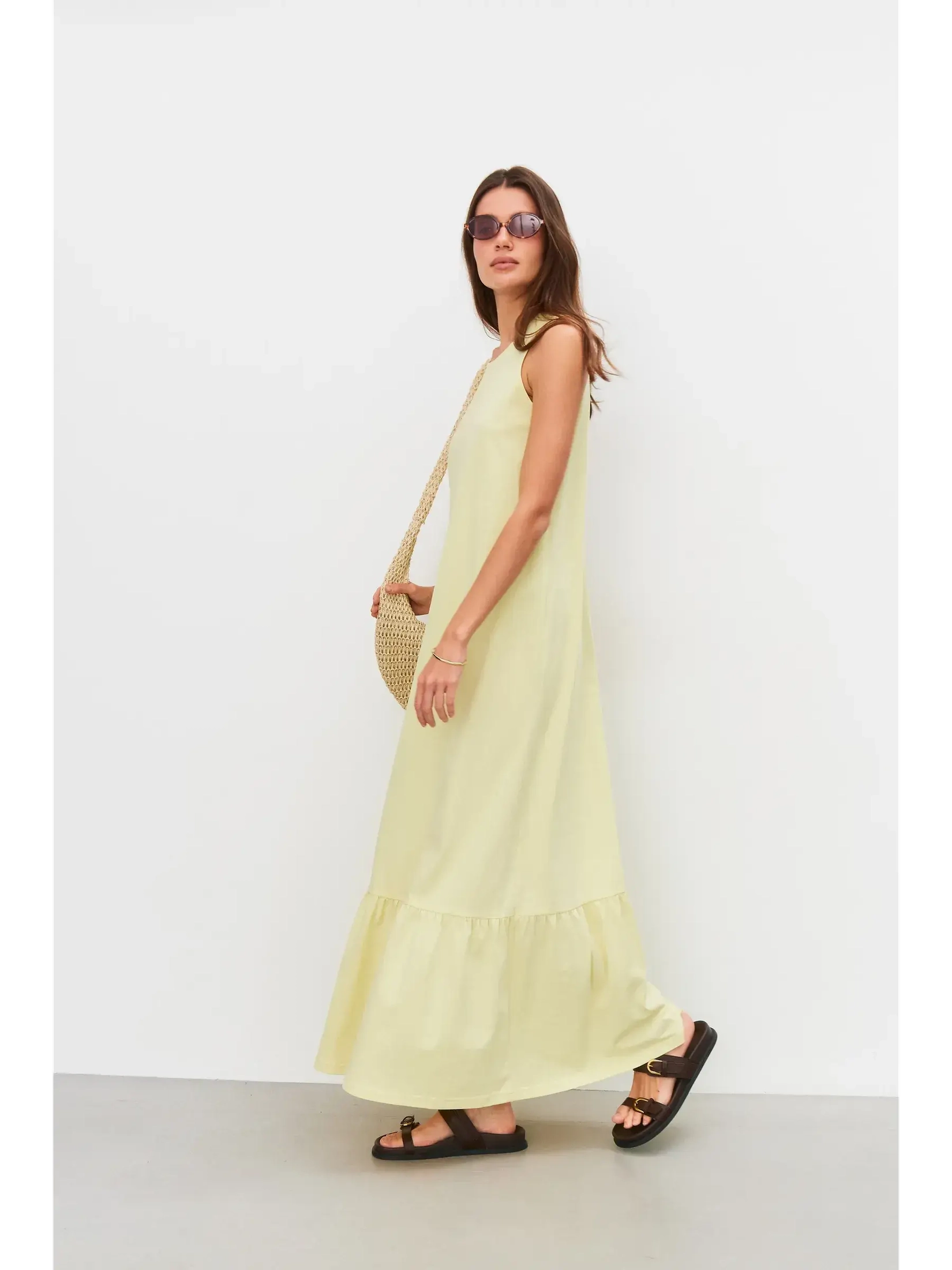 Model wearing a sleeveless light lemon Sunrise Maxi Dress with flounce hem, styled for summer outings.