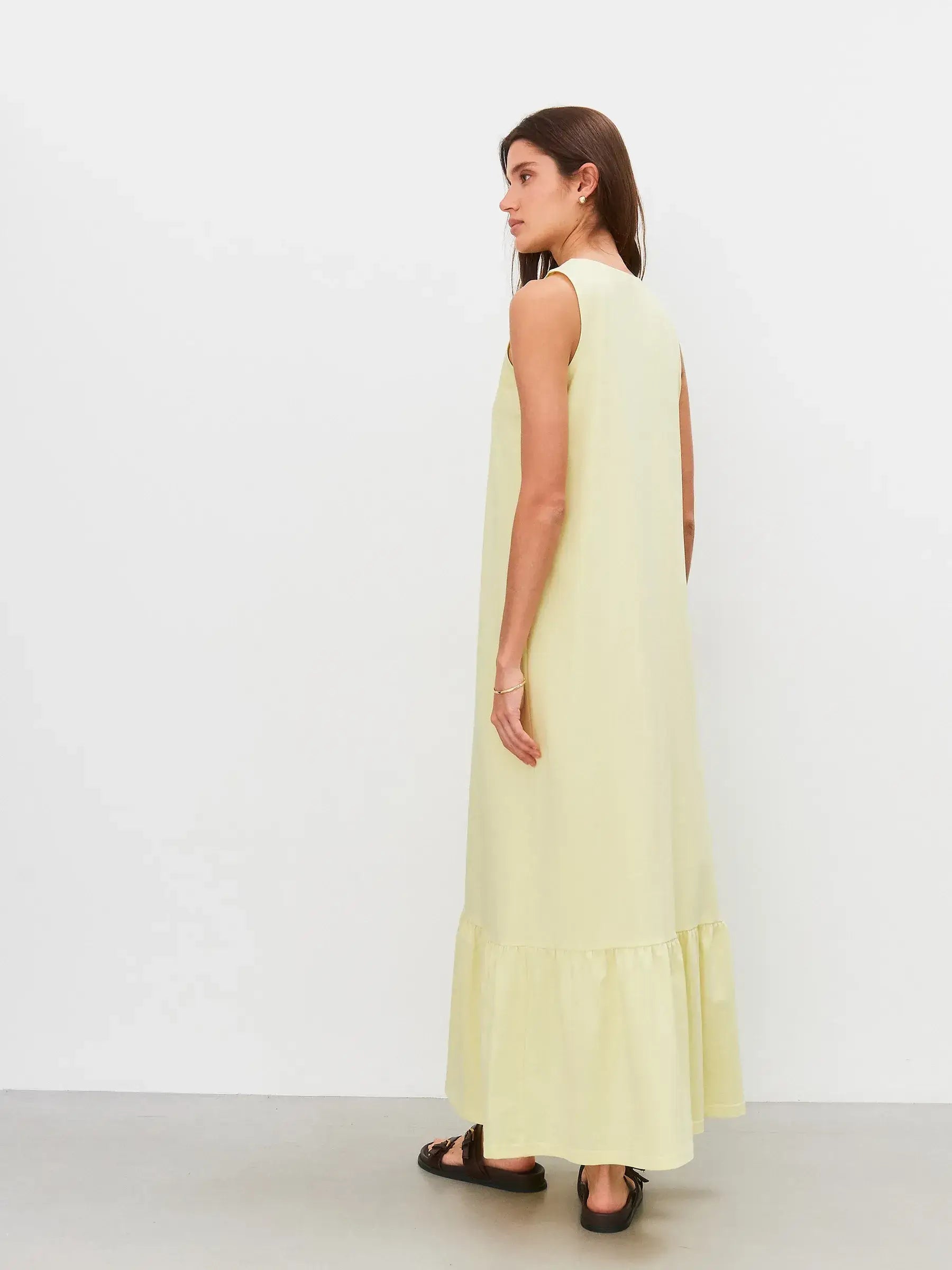 Back view of a woman in a sleeveless light lemon Sunrise Maxi Dress with gathered hem flounce.