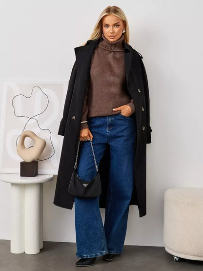Woman wearing Terra Sweater by Lauven, an oversized brown knit turtleneck paired with a black coat and blue jeans.