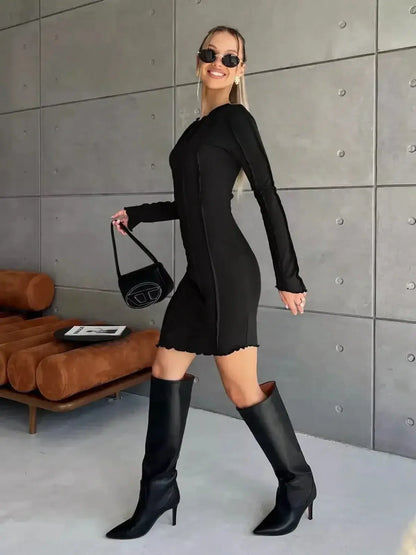 Model in a black mini dress with long sleeves and knee-high boots, showcasing a chic and edgy style.