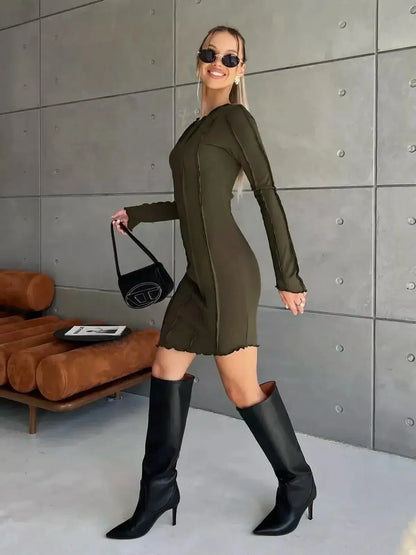 Olive green long sleeve mini dress with contrast stitching, styled with knee-high boots and sunglasses.