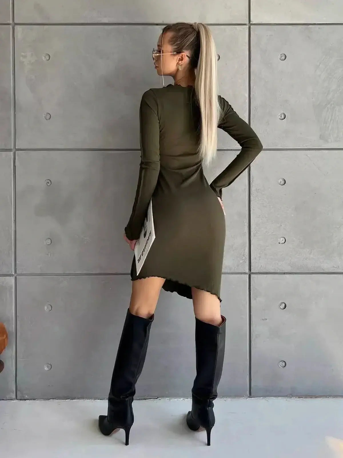 Olive green long sleeve mini dress with asymmetrical hem, styled with knee-high boots and modern sunglasses.