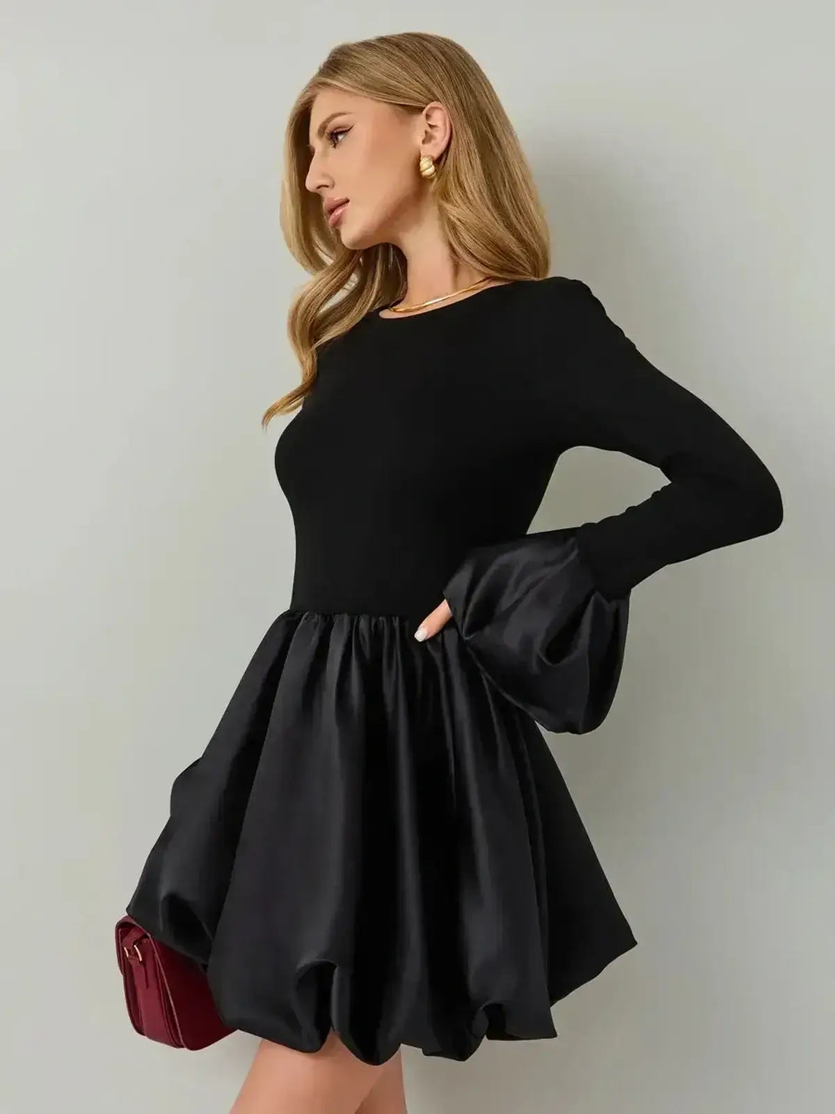 Model wearing Velvet Bloom black mini dress with soft knit bodice and satin balloon skirt, featuring long sleeves and exaggerated cuffs.
