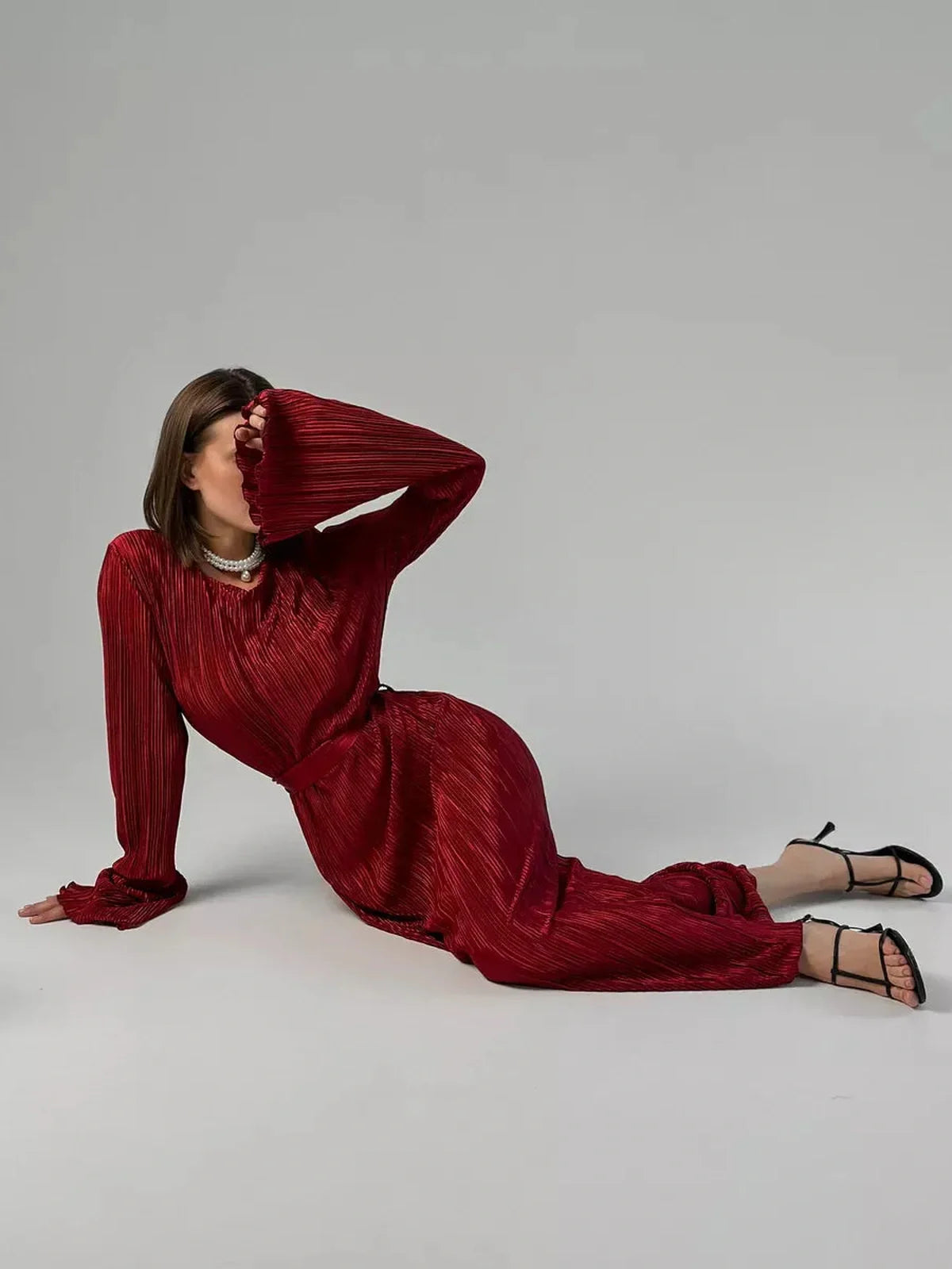 Model wearing the Velvet Flame Maxi Dress in glossy marsala red with pleats, flared sleeves, and a dramatic silhouette.