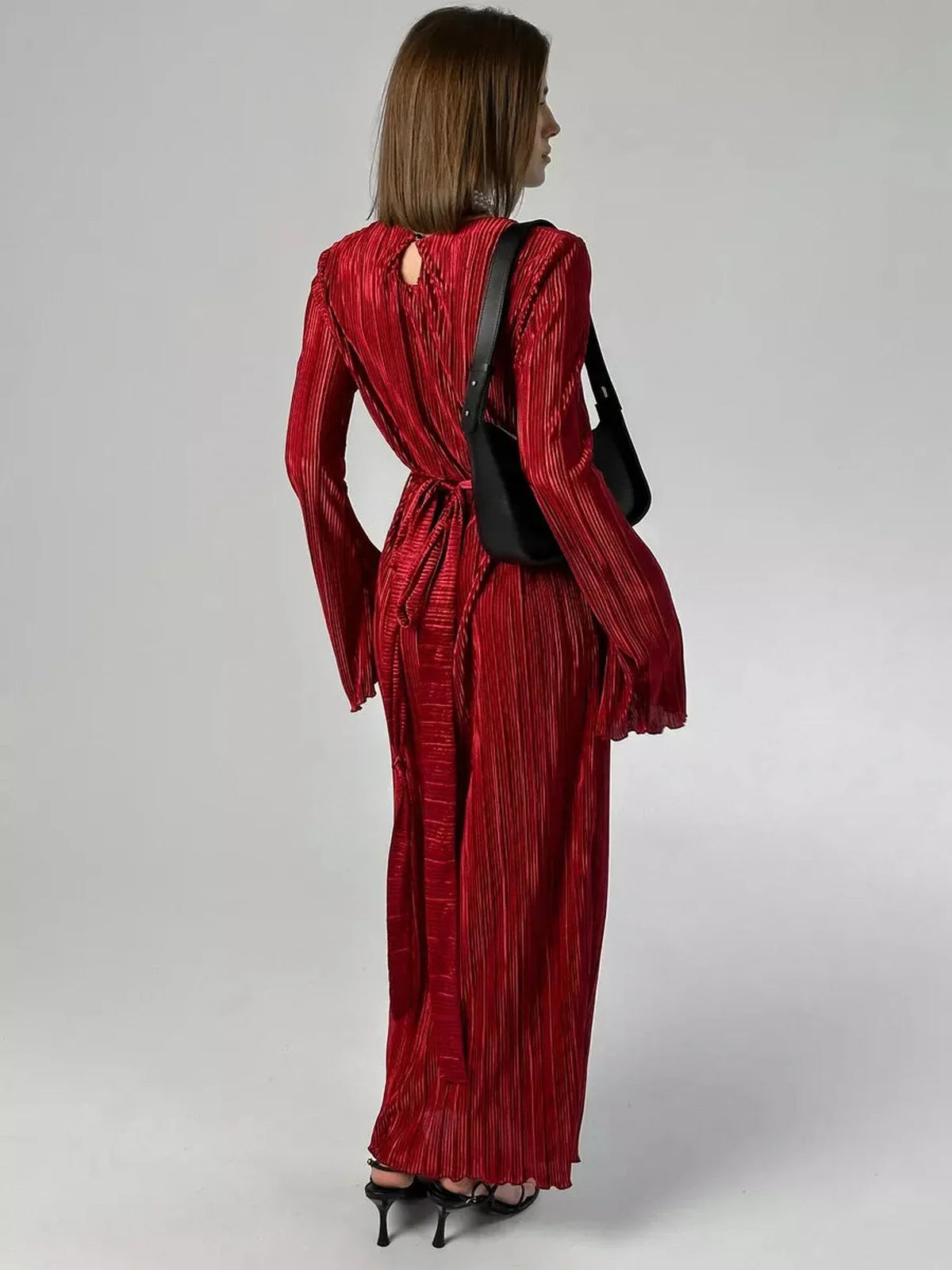 Woman in a glossy marsala red Velvet Flame Maxi Dress showcasing flared sleeves and pleated texture.
