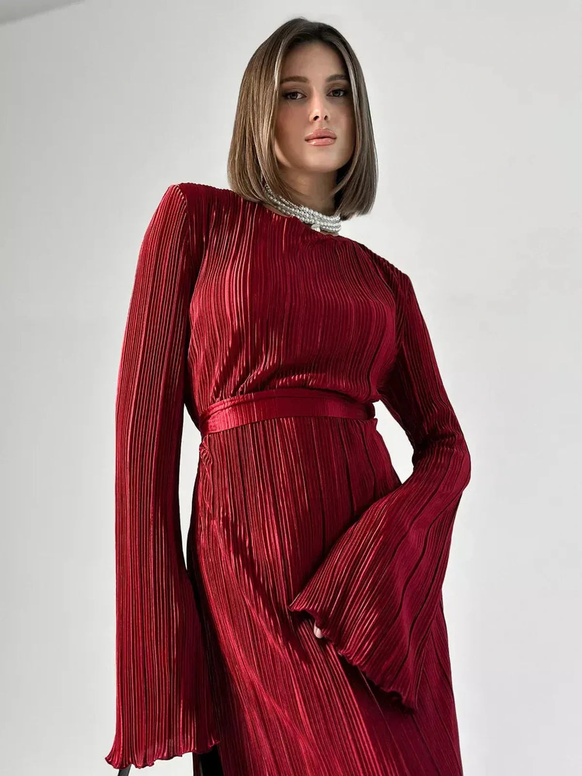 Model wearing Velvet Flame Maxi Dress in glossy marsala red with pleats and flared sleeves, showcasing elegant evening wear.