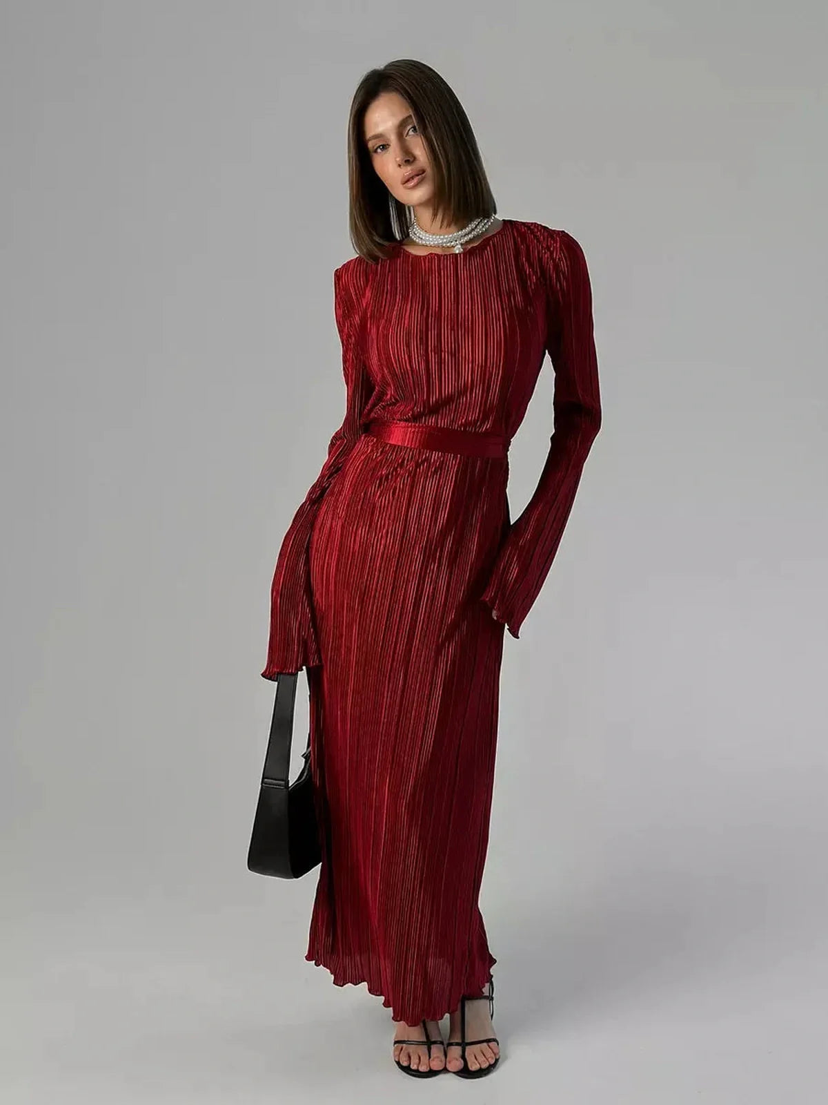 Model showcasing the Velvet Flame Maxi Dress in glossy marsala red, featuring pleats and a removable belt for waist definition.
