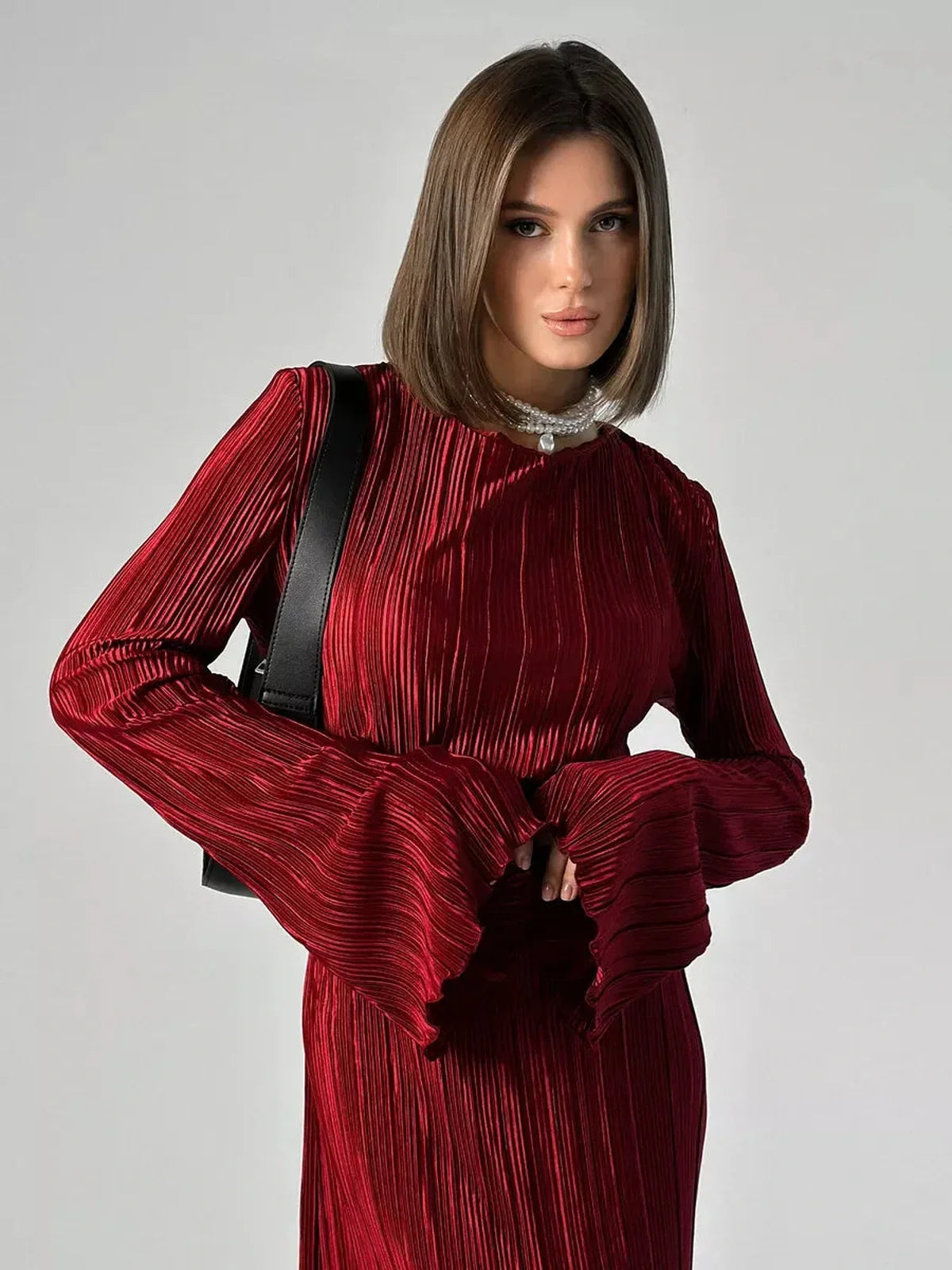 Model wearing the Velvet Flame Maxi Dress in glossy marsala with pleated design and flared sleeves.
