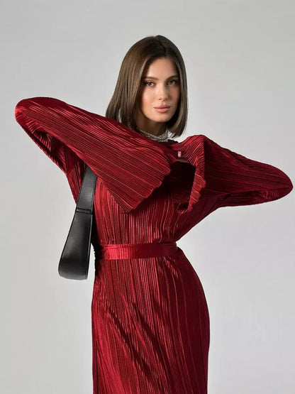 Model showcasing the Velvet Flame Maxi Dress in glossy marsala red with flared sleeves and pleated texture.