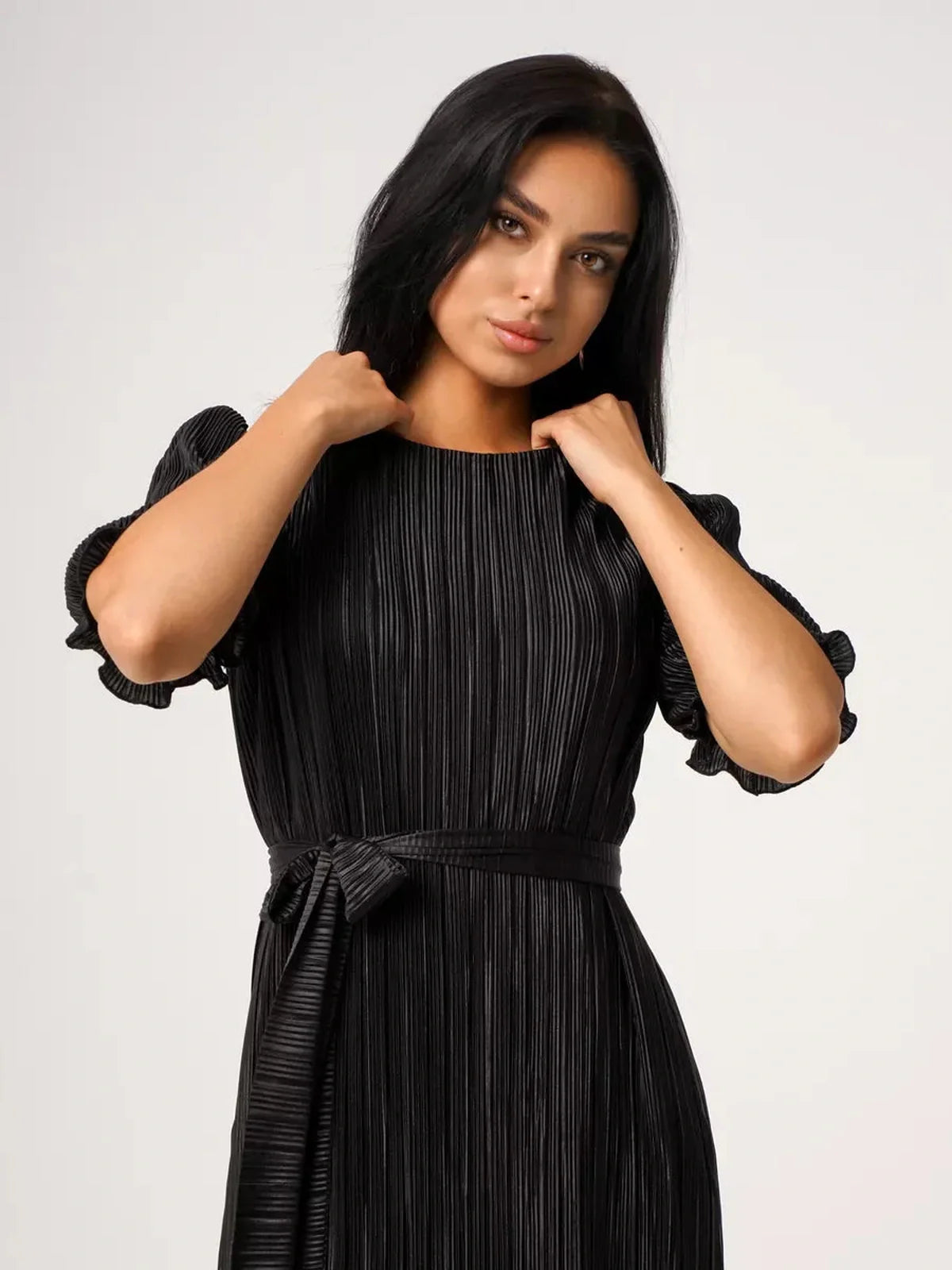 Elegant woman in black pleated Velvet Rhythm Maxi Dress with puff sleeves and sash belt for stylish occasions.