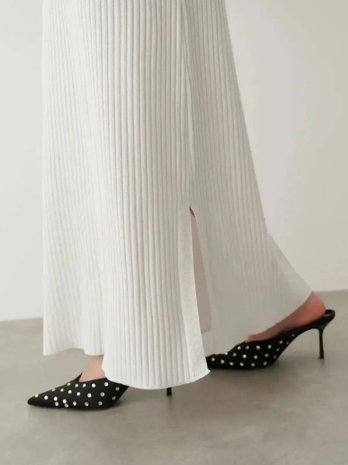 Detail of the Verona Maxi Dress showcasing its ribbed texture and side slit, paired with stylish black polka dot heels.