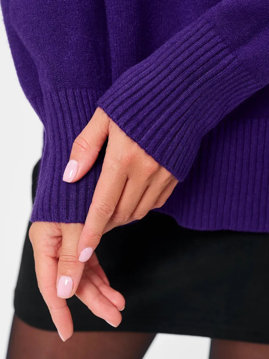 Close-up of hands wearing the Violet Sweater by Lauven, showcasing the ribbed cuffs and deep purple color.