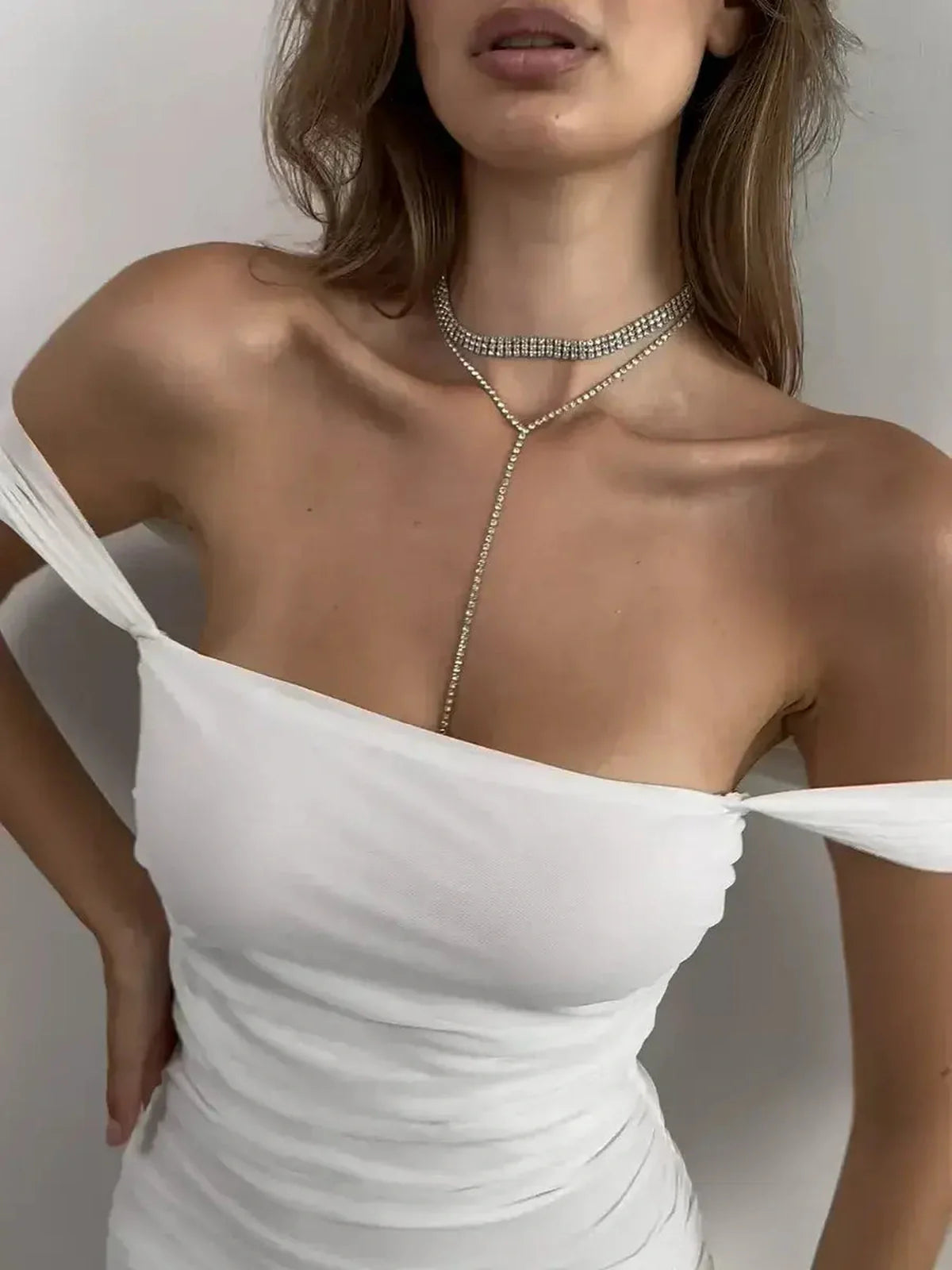 Close-up of a model wearing a stylish off-shoulder white dress adorned with a sparkling choker necklace.