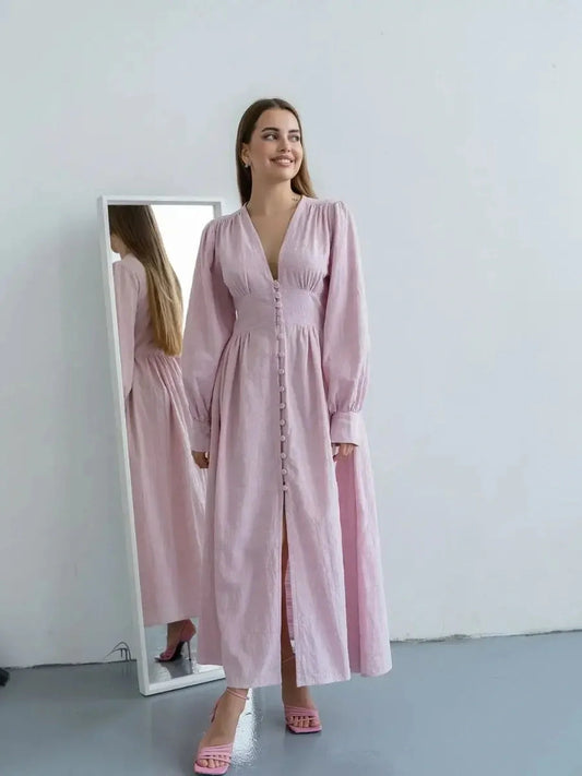 Young woman in Willow Grace Maxi Dress, a soft pink cotton gown with a V-neckline and button-front detail.