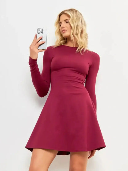 Elegant woman wearing the Wine Flare Mini dress in burgundy, showcasing a flattering silhouette and long sleeves.