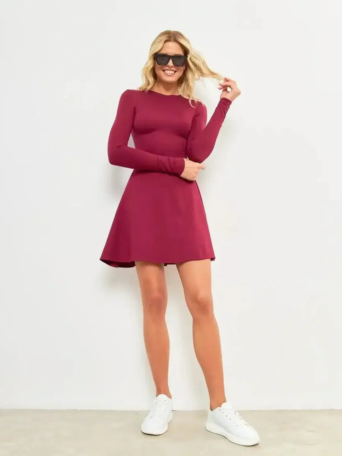Model wearing a burgundy Wine Flare Mini dress with long sleeves, styled casually with white sneakers.